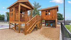 A wooden play structure with a slide and climbing wall, surrounded by a fenced area. - Lakescape at The Getaways (Kimberling City)