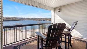 A balcony with a view of a lake and hills, featuring two Adirondack chairs and a lantern. - Lakescape at The Getaways (Kimberling City)