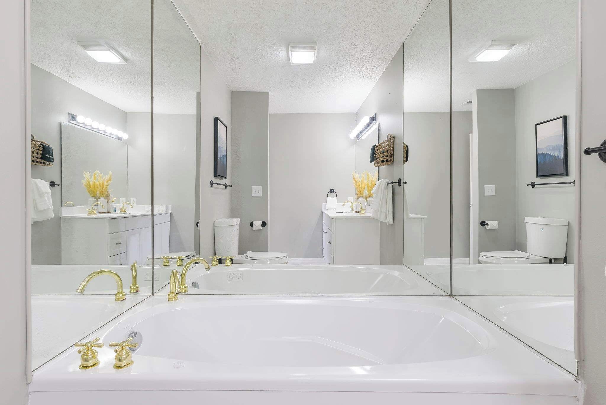 A modern bathroom with a large white bathtub, a vanity with a mirror, and a toilet.