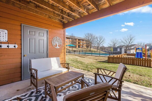 An outdoor patio with wooden furniture, a door, and a view of a pool and playground in the background. - Pointe Royale Retreat - Relaxation Awaits! (Branson)