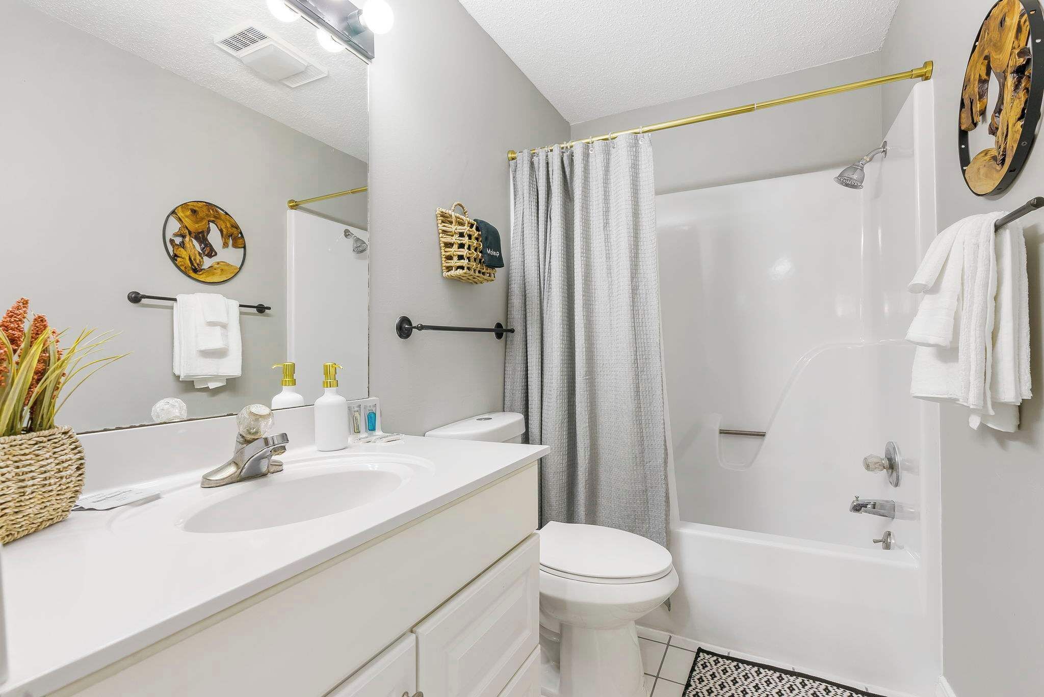 Un baño moderno con lavamanos, inodoro y bañera blancos. Hay una cortina de ducha, un perchero y una pequeña cesta con toallas.