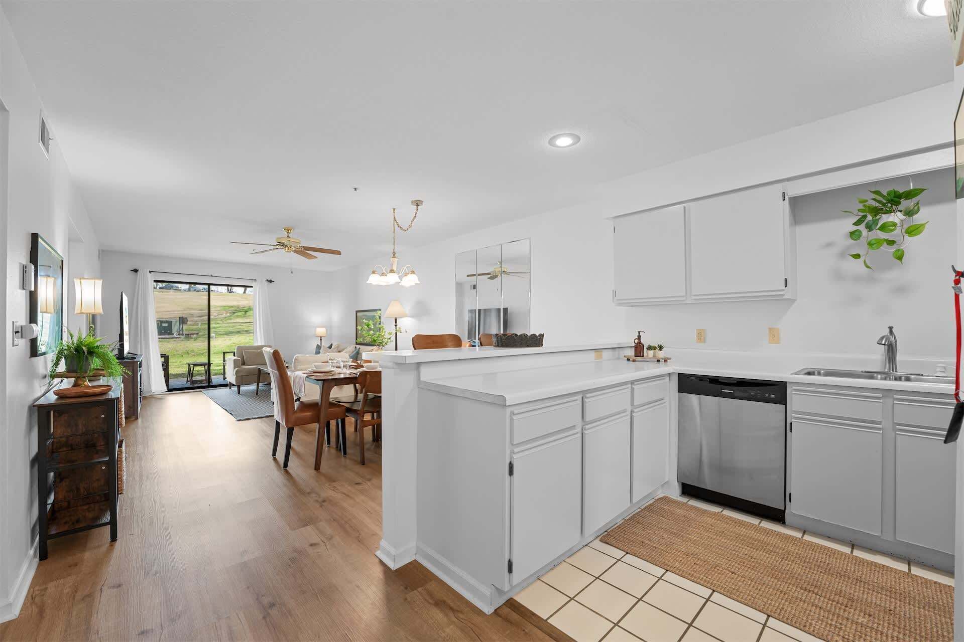 A modern kitchen with white cabinetry, a dishwasher, and a dining area with a table and chairs.