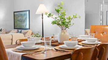 A dining area with a table set for four, a vase with green foliage, and a lamp.