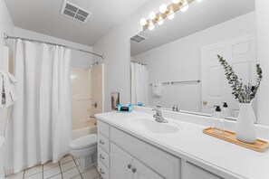 A modern bathroom with a shower, toilet, vanity with a mirror, and a sink. - Royal Ridge Modern Condo for 4 (Branson)
