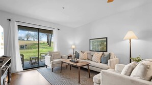 A living room with a sofa, coffee table, and a view of a grassy area through a sliding glass door. - Royal Ridge Modern Condo for 4 (Branson)