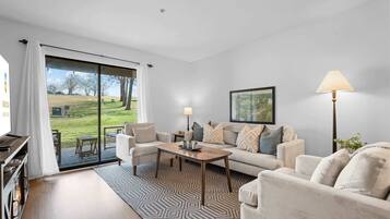 A living room with a sofa, coffee table, and a view of a grassy area through a sliding glass door.