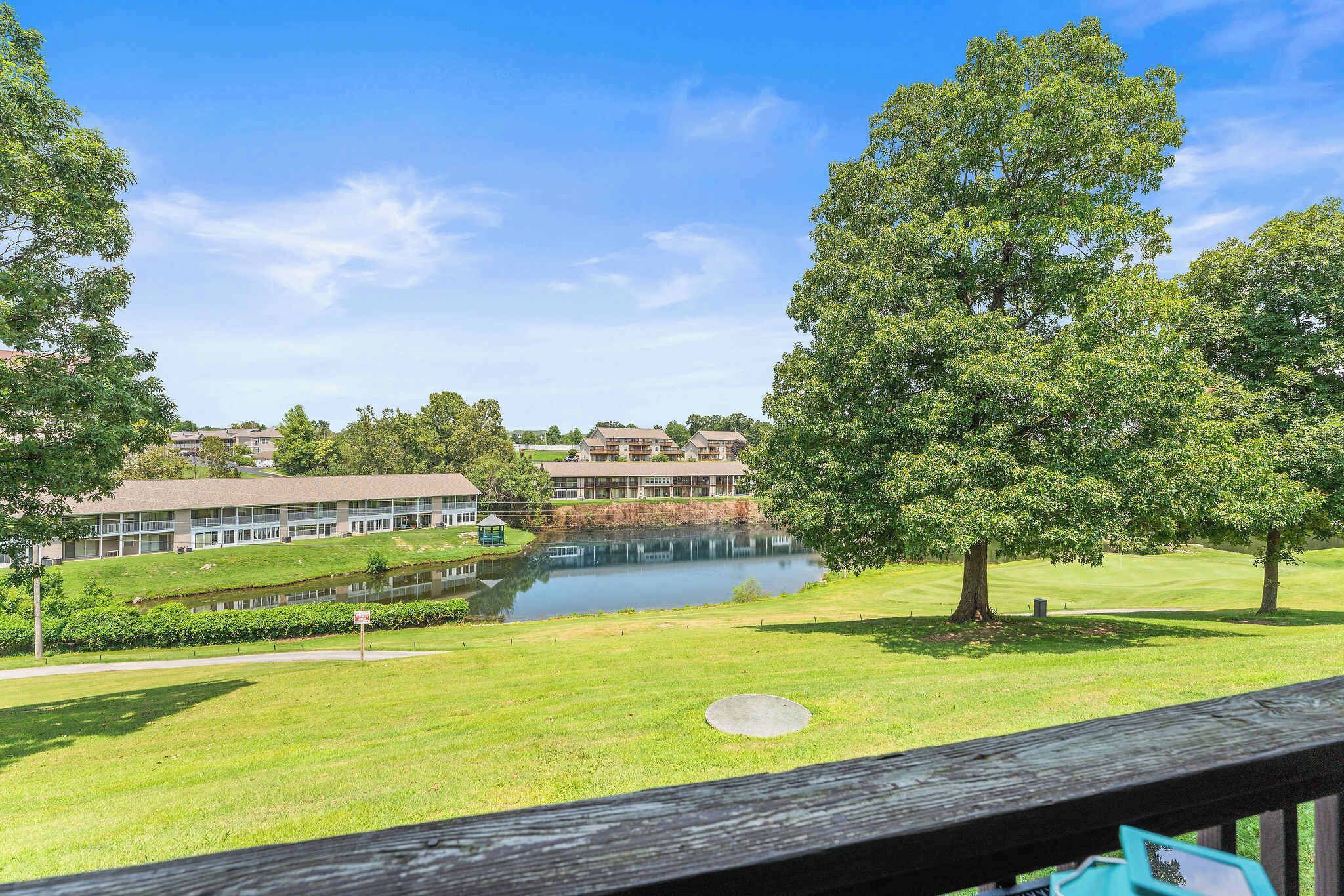 A view of a golf course with a pond, trees, and buildings in the background.