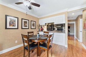 A dining area with a round table and chairs, a ceiling fan, framed artwork on the wall, and a kitchen in the background. - Pointe Royale Getaway - Fore 4 (Branson)