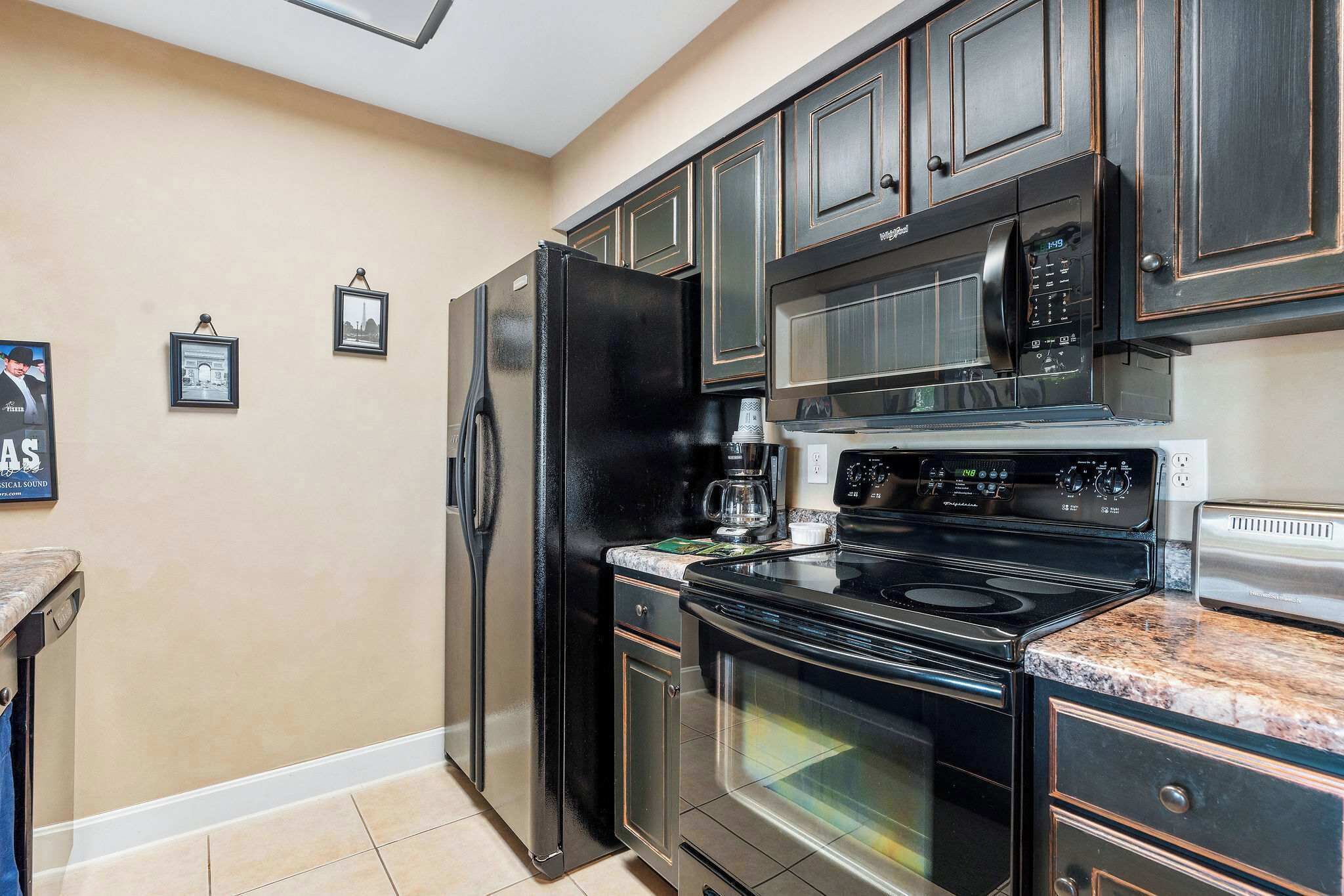 A kitchen with dark cabinets, a black refrigerator, a microwave, a stove, and a coffee maker.