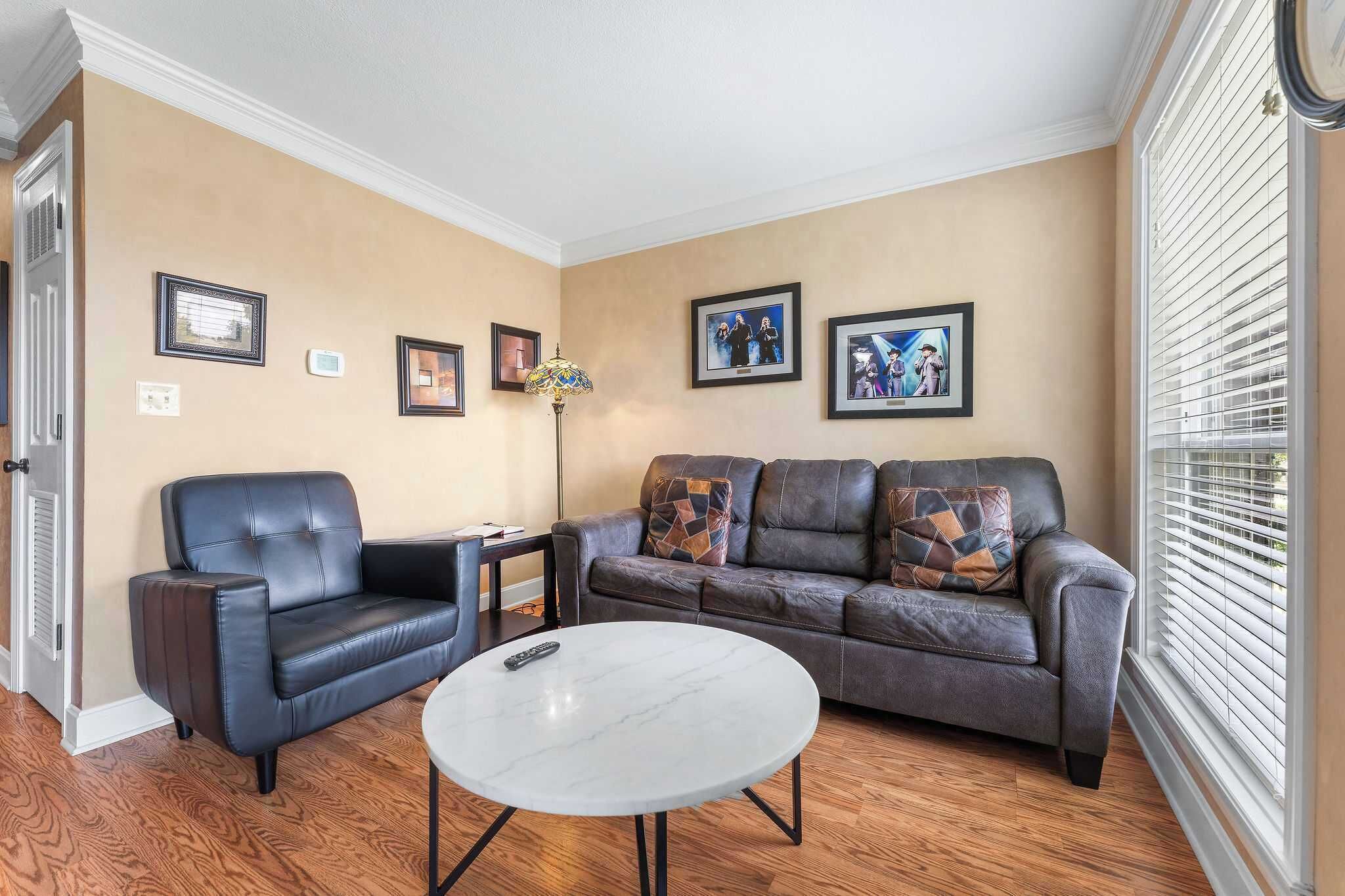 Un salon avec un canapé, un fauteuil, une table basse et des tableaux encadrés accrochés au mur.