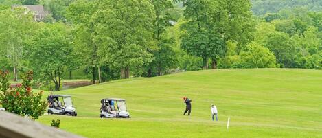 Un campo de golf con un club house, un putting green y una colina boscosa al fondo.