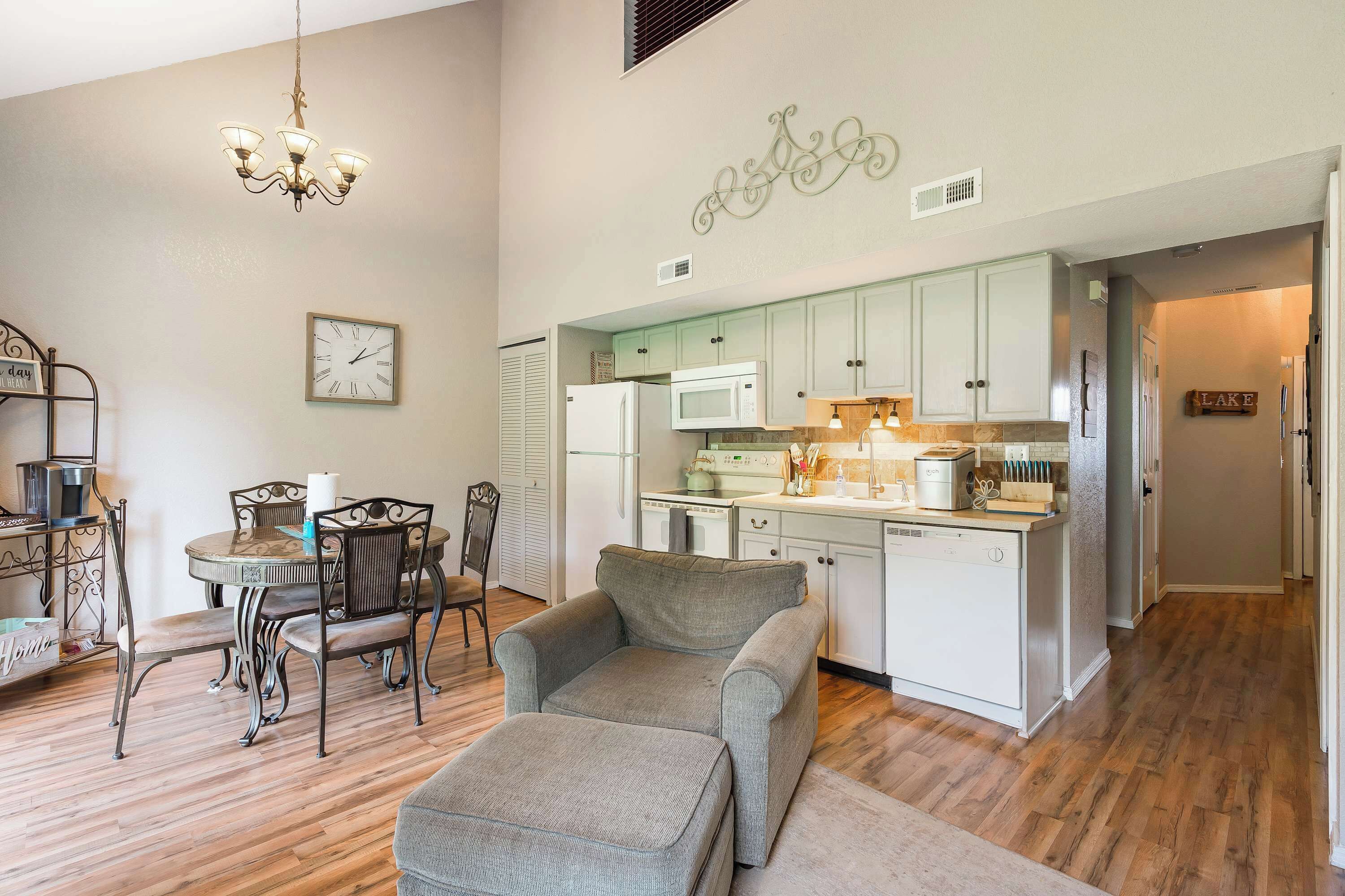 A modern kitchen with white cabinets, a microwave, and a dishwasher. There is a dining area with a table and chairs, and a chandelier hanging above.