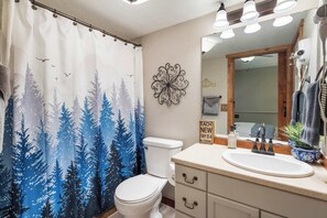 Ein Badezimmer mit Duschvorhang mit Waldmotiv, einer weißen Toilette, einem Waschbecken mit Spiegel und einer Wanddekoration.