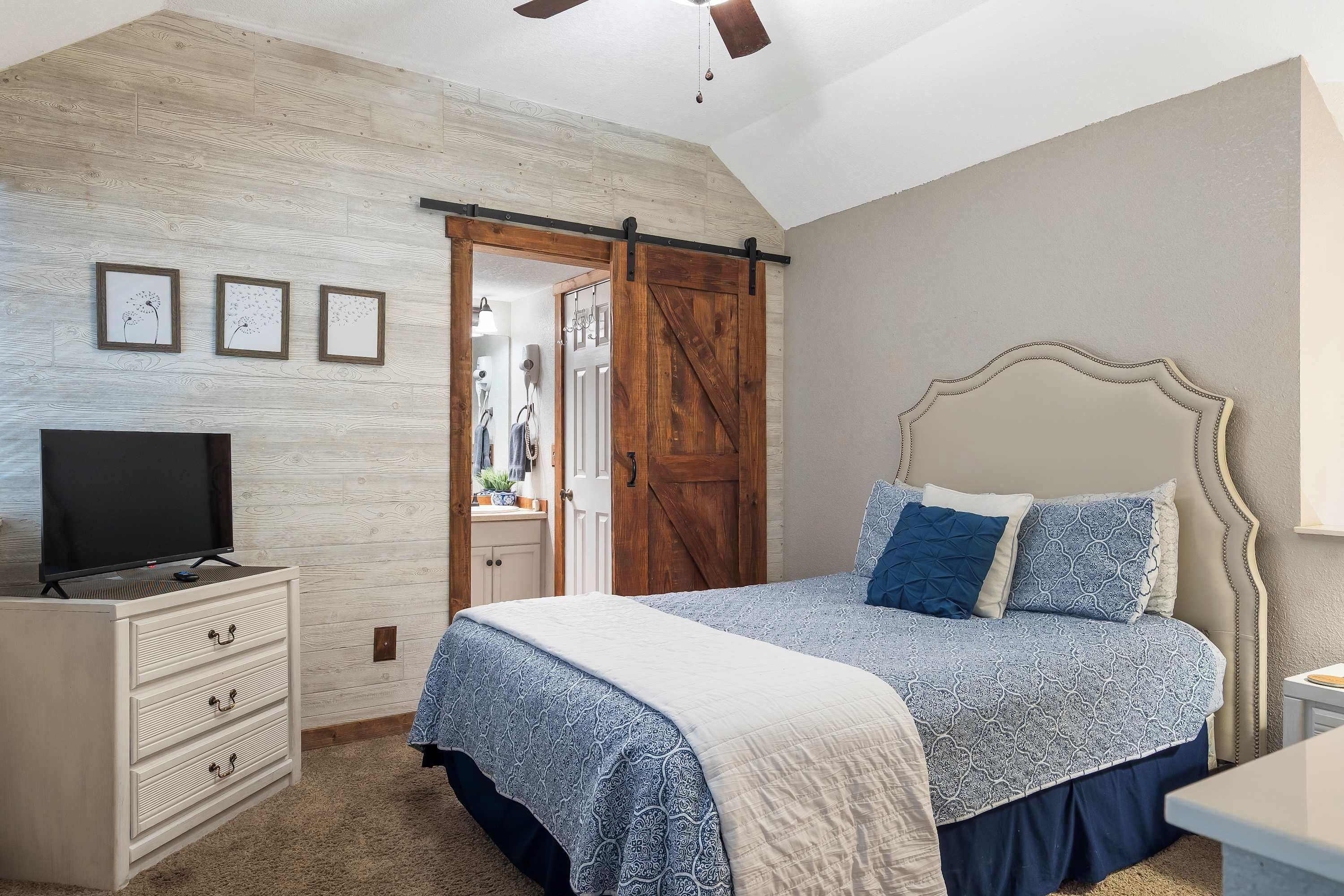 Ein Schlafzimmer mit Bett, Schminktisch, Fernseher und einer Schiebetür im Bauernhausstil.
