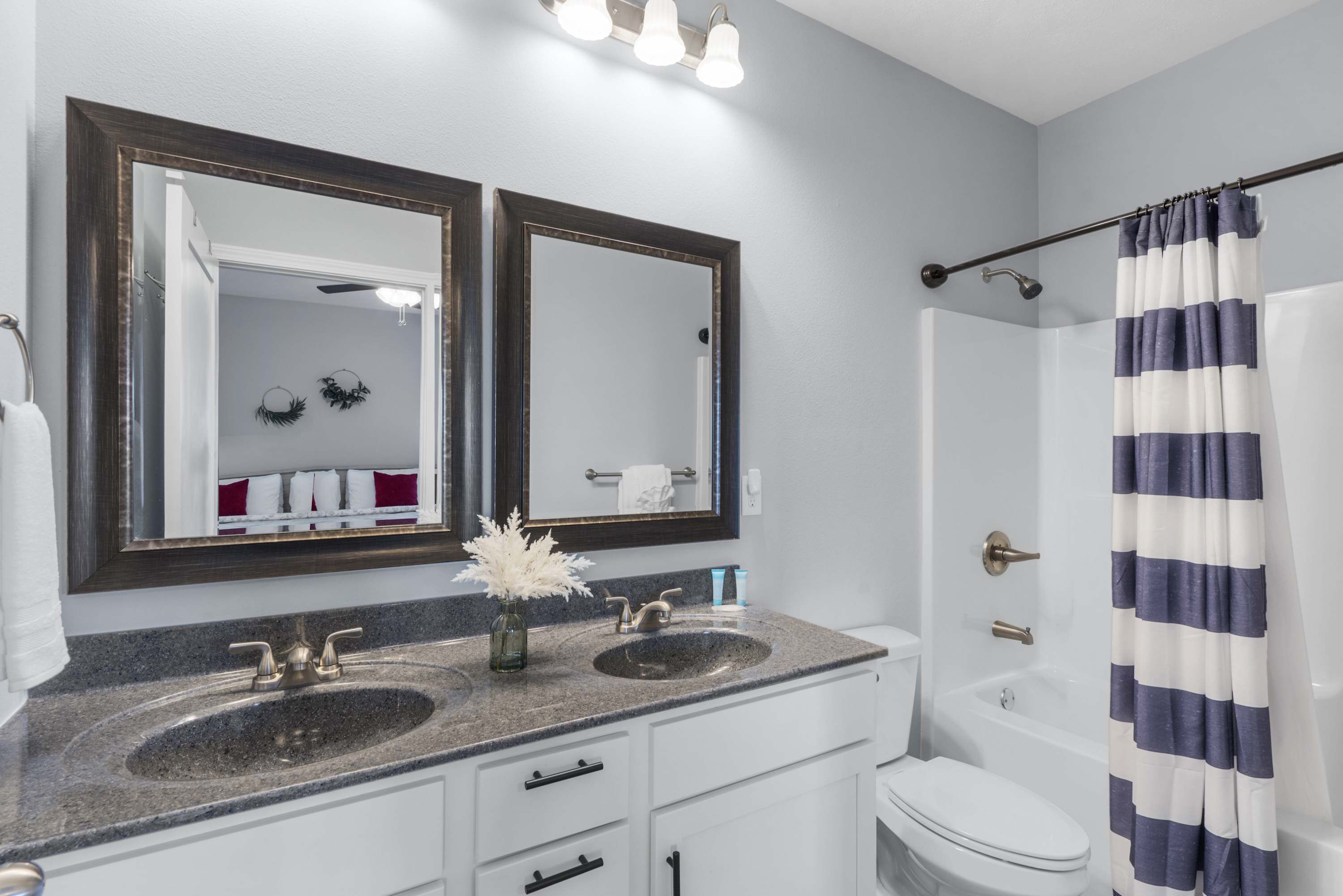 Une salle de bain avec deux lavabos, des toilettes et une douche. Il y a deux miroirs au-dessus des lavabos et un porte-serviettes avec des serviettes.