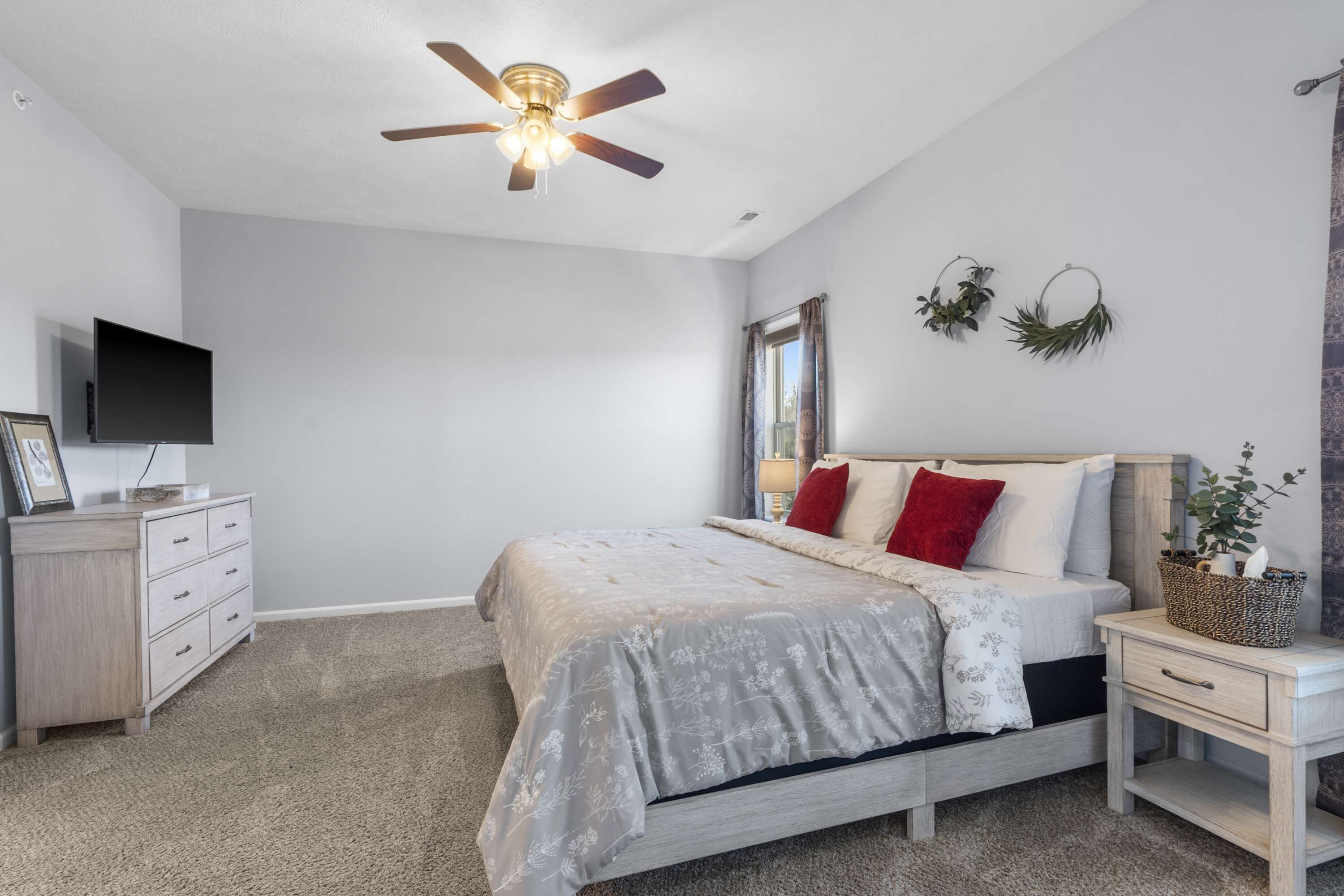 A bedroom with a bed, a ceiling fan, a TV, a dresser, and a nightstand with a plant.