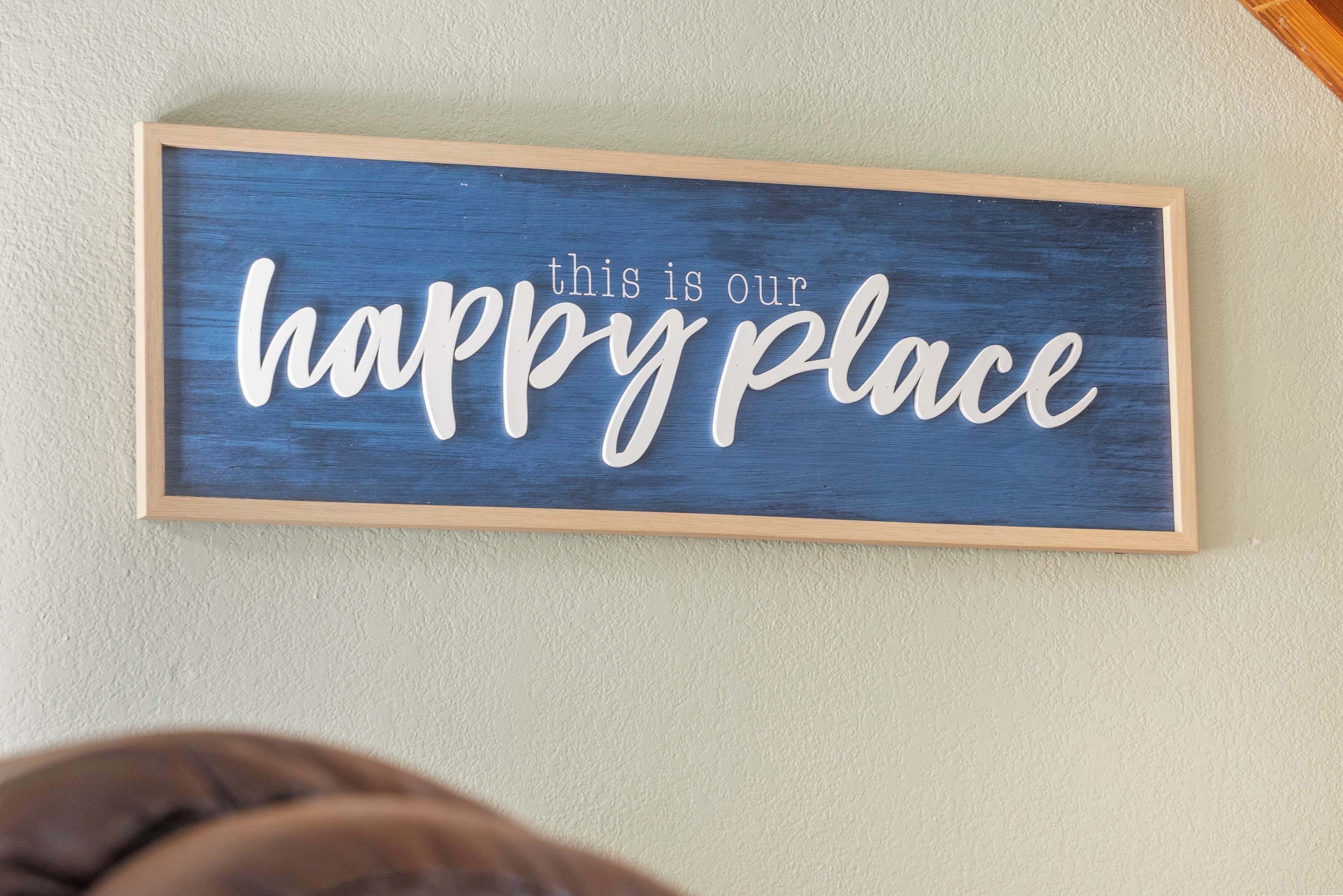 A framed sign with the text "this is our happy place" on a textured wall.