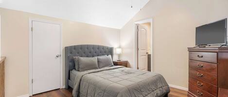 Een slaapkamer met een bed, dressoir, plafondventilator en een televisie.