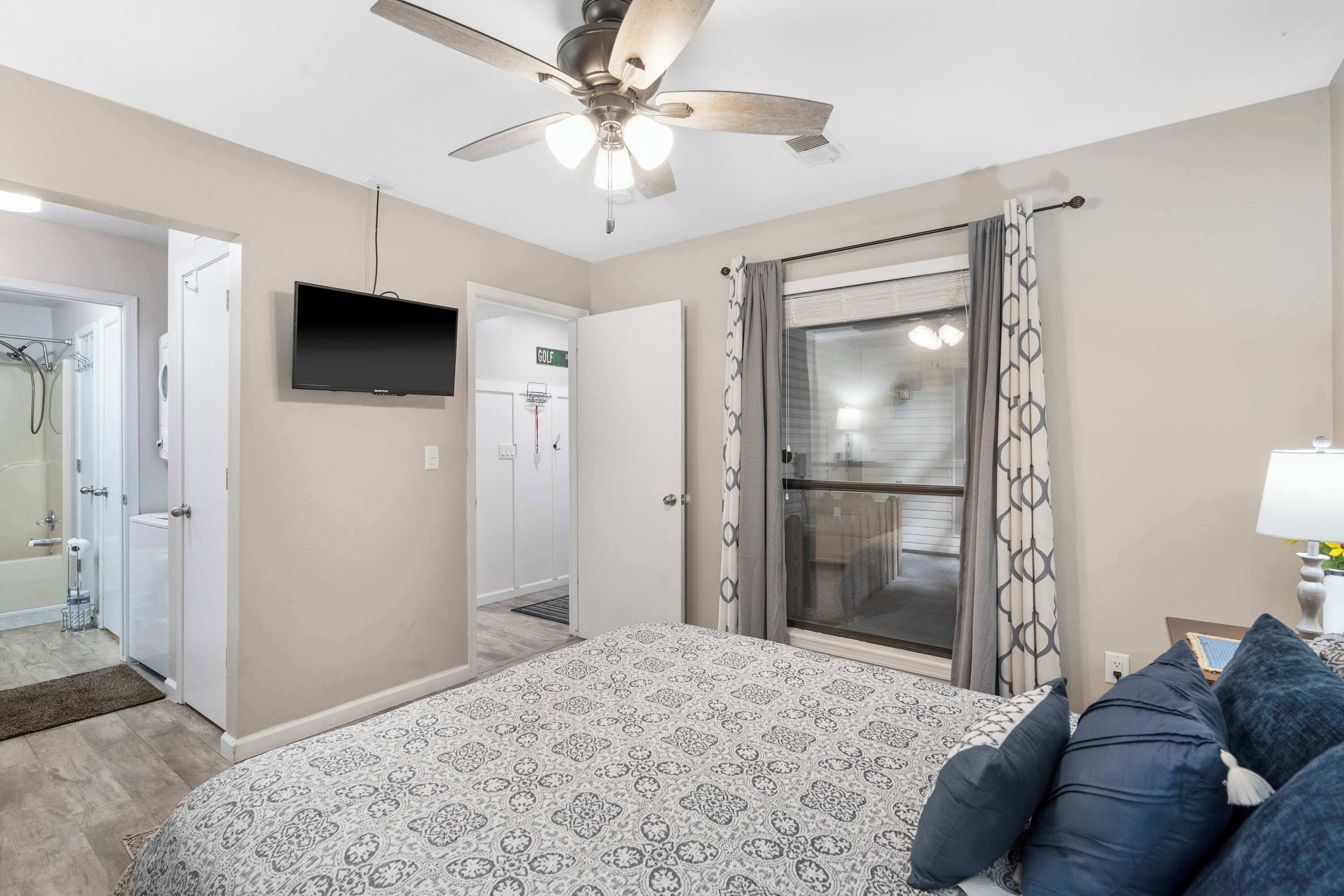 Une chambre à coucher comprenant un lit, un ventilateur de plafond, une télévision et une salle de bain avec douche et toilettes.