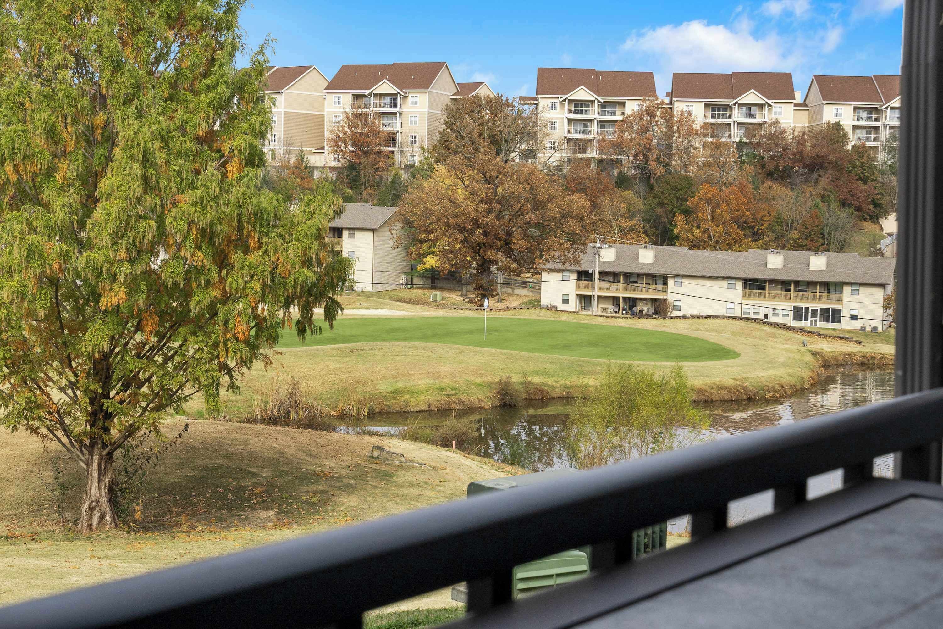 Vista de un campo de golf con un estanque, rodeado de árboles y edificios residenciales.