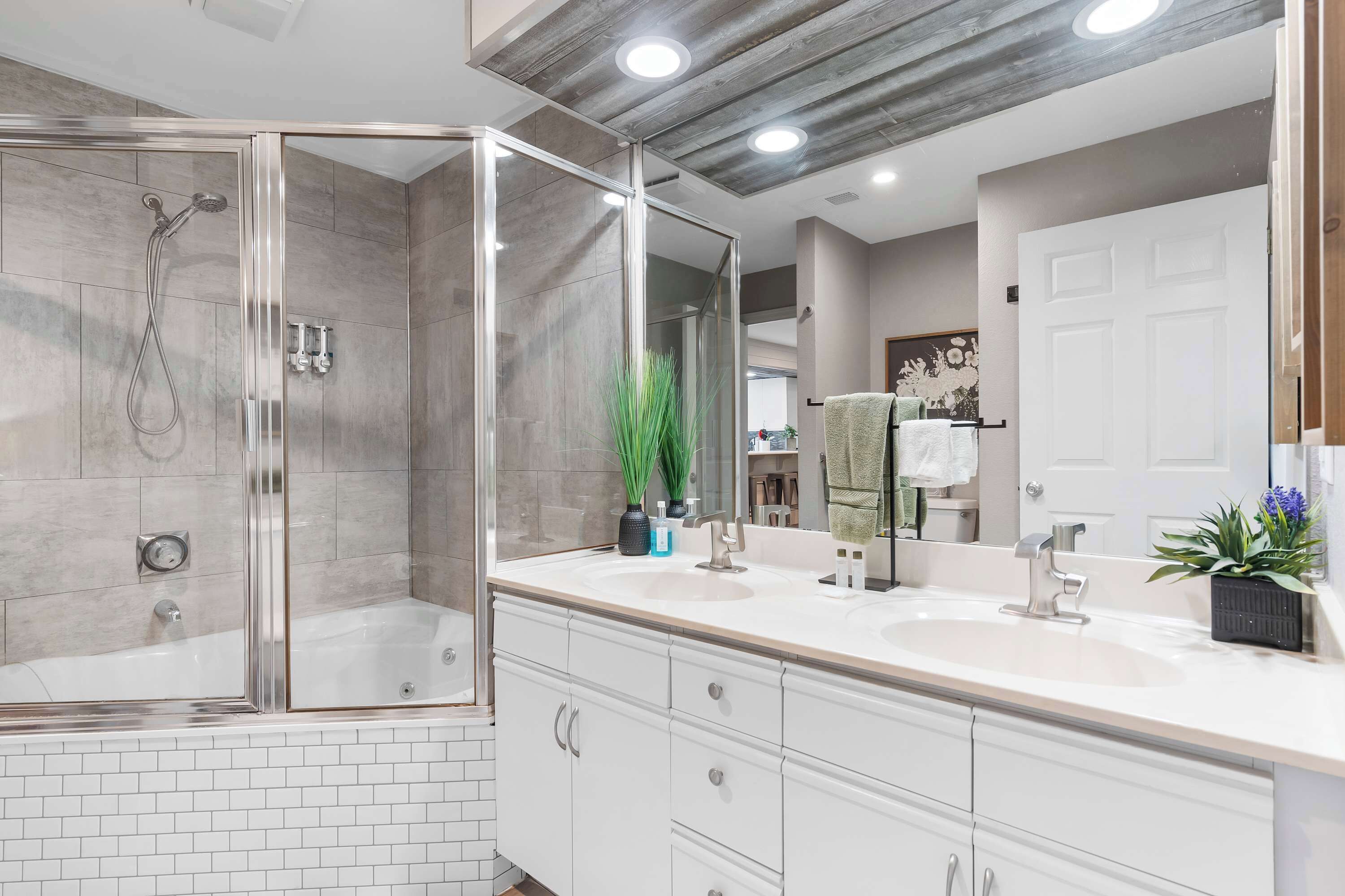 A modern bathroom with a glass-enclosed shower, a large mirror, and a white vanity with drawers.