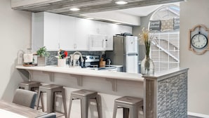 A modern kitchen with white cabinets, a central island with stools, a built-in oven, and a refrigerator. - Lakeside Bliss Retreat 2 BDR (Branson)