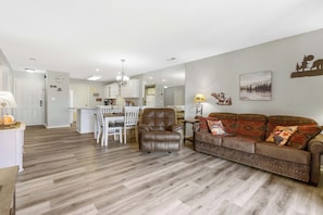 A living room with a leather armchair, a brown sofa, a dining table with chairs, a kitchen area, and a hallway leading to a bedroom. - Ozark Escape at the Pointe - Epic Nature (Branson)