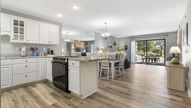 A modern kitchen with white cabinetry, a central island, and a dining area with chairs.