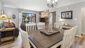 A dining area with a wooden table, white chairs, a chandelier, and a fireplace.