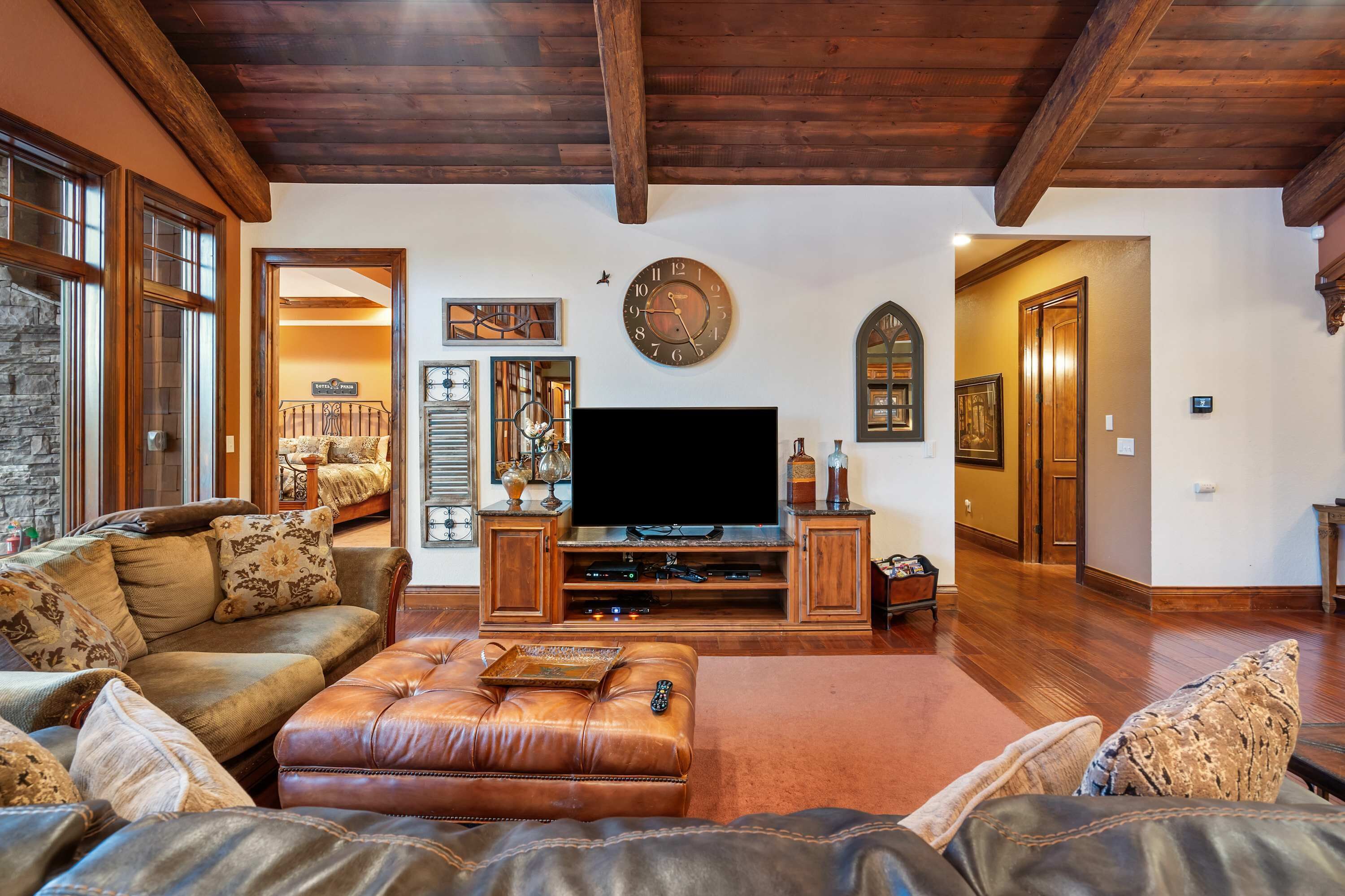 A spacious living room with a large flat-screen TV, leather sofas, wooden entertainment unit, and a stone wall.