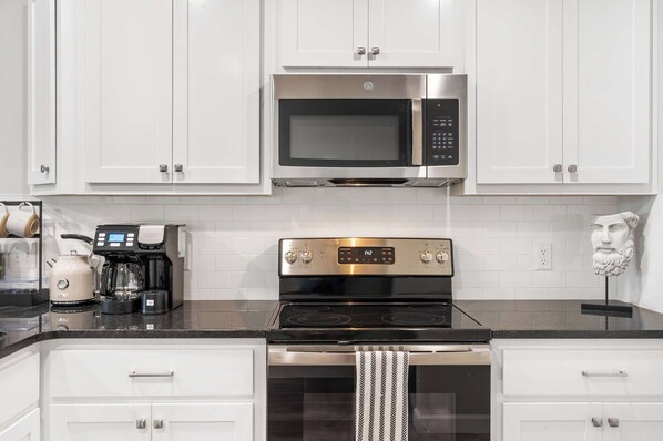 A modern kitchen with white cabinets, a stainless steel microwave, a coffee maker, and a gas stove. - Earl Grey Escape - Chic 3 Bdr! (Branson)