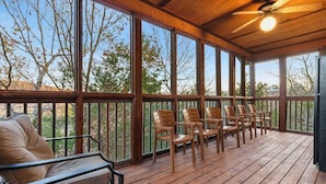 A covered outdoor seating area with wooden chairs and a cushioned bench, large windows, and a ceiling fan. - Kemper's Cabin in the Ozarks - Onsite Amenities (Branson)