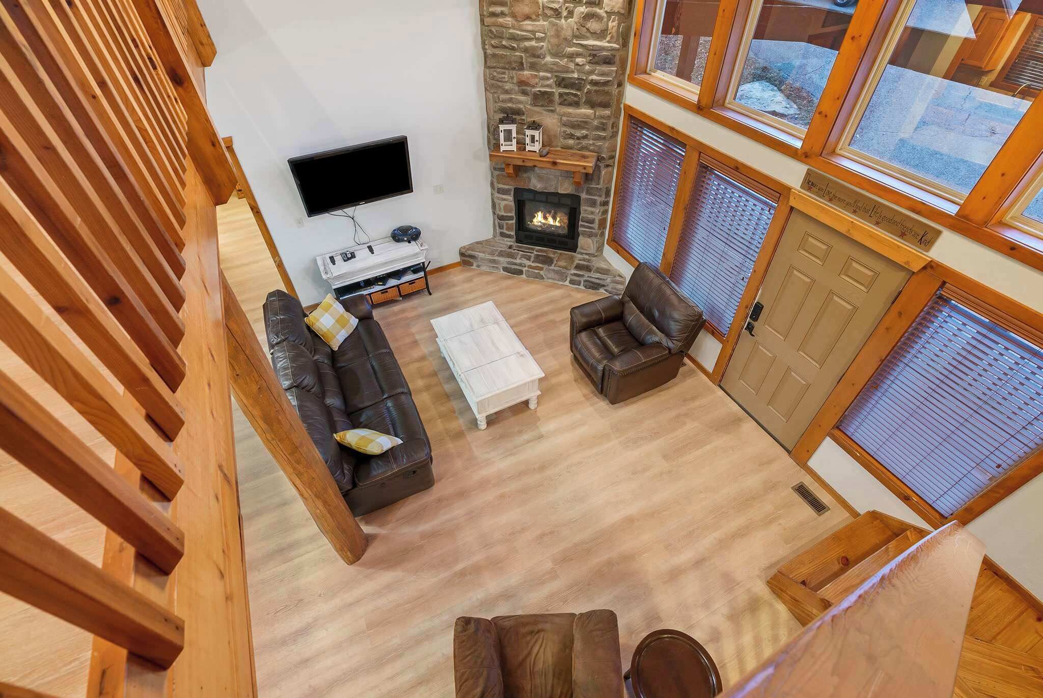A living room with a stone fireplace, wooden beams, a flat-screen TV, and leather sofas.