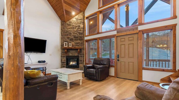 A spacious living room with a stone fireplace, leather furniture, and large windows. - Kemper's Cabin in the Ozarks - Onsite Amenities (Branson)