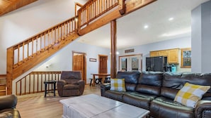 A spacious living room with a wooden staircase, leather sofas, and a dining area. - Kemper's Cabin in the Ozarks - Onsite Amenities (Branson)