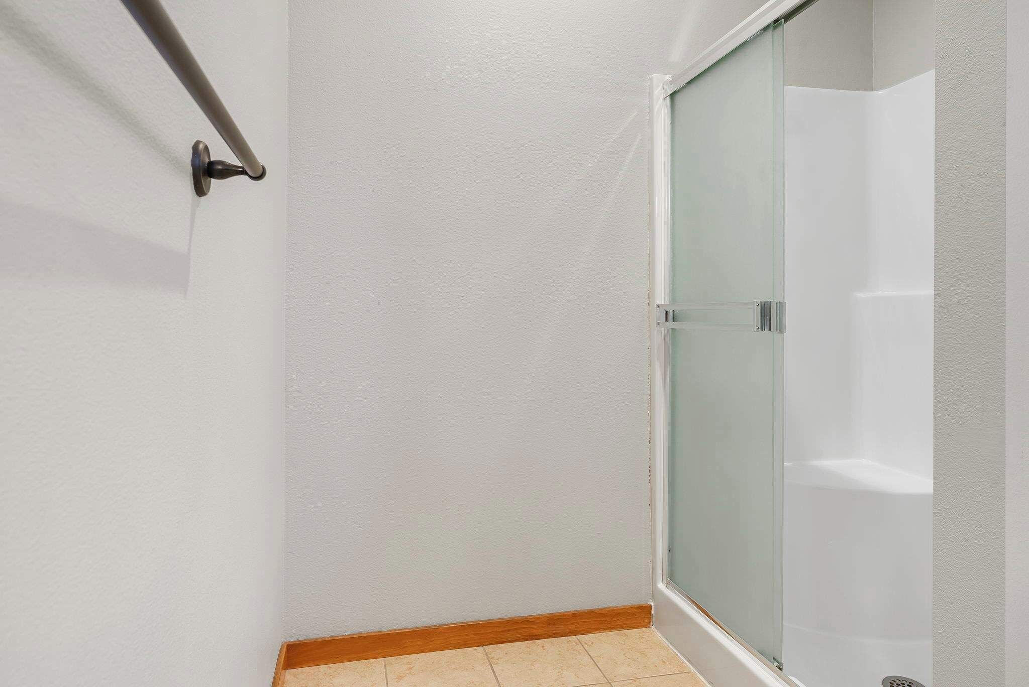 A corner of a room with a glass shower door, a wooden baseboard, and a white wall.