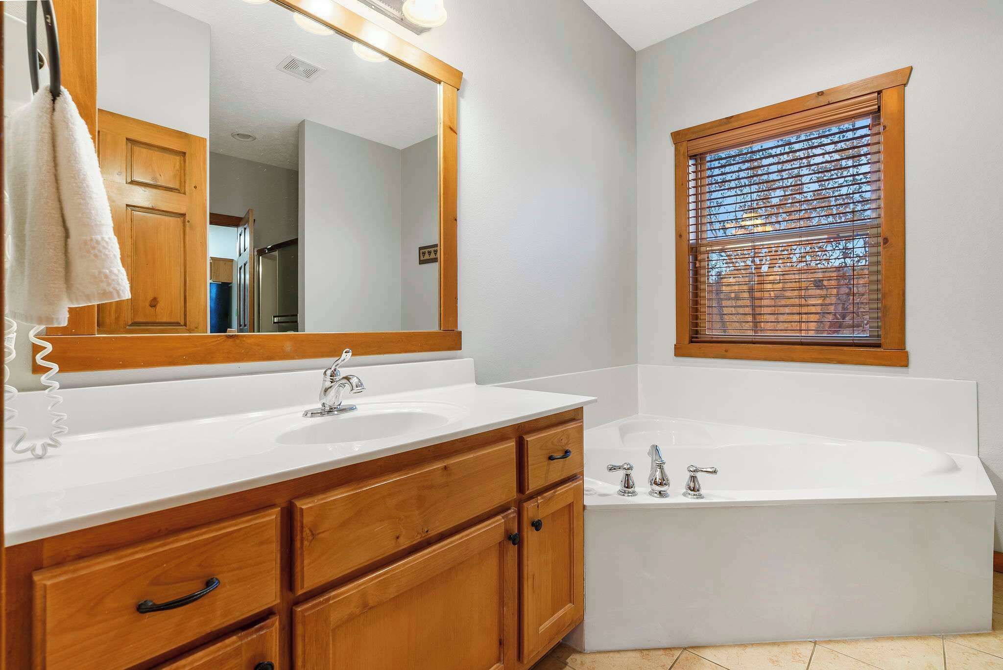 Un baño con tocador de madera, un espejo grande, una bañera y una ventana con persianas.