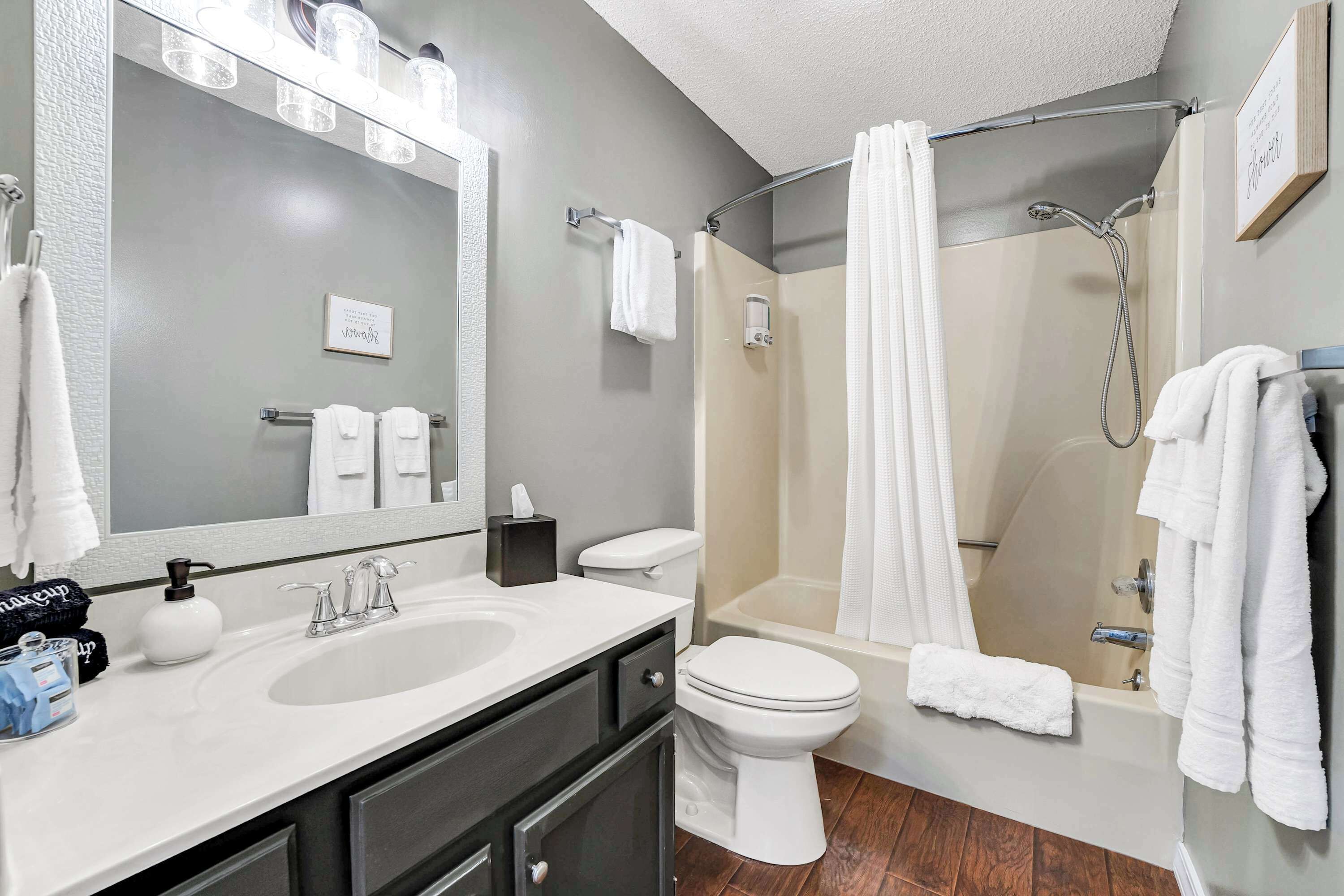 A bathroom with a sink, toilet, and shower. There are towels hanging on the wall and a mirror above the sink.