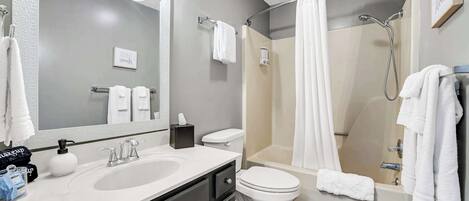 A bathroom with a sink, toilet, and shower. There are towels hanging on the wall and a mirror above the sink.