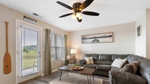 Un salon avec un canapé en cuir foncé, une table basse en bois, un ventilateur de plafond et une porte donnant sur l’extérieur.