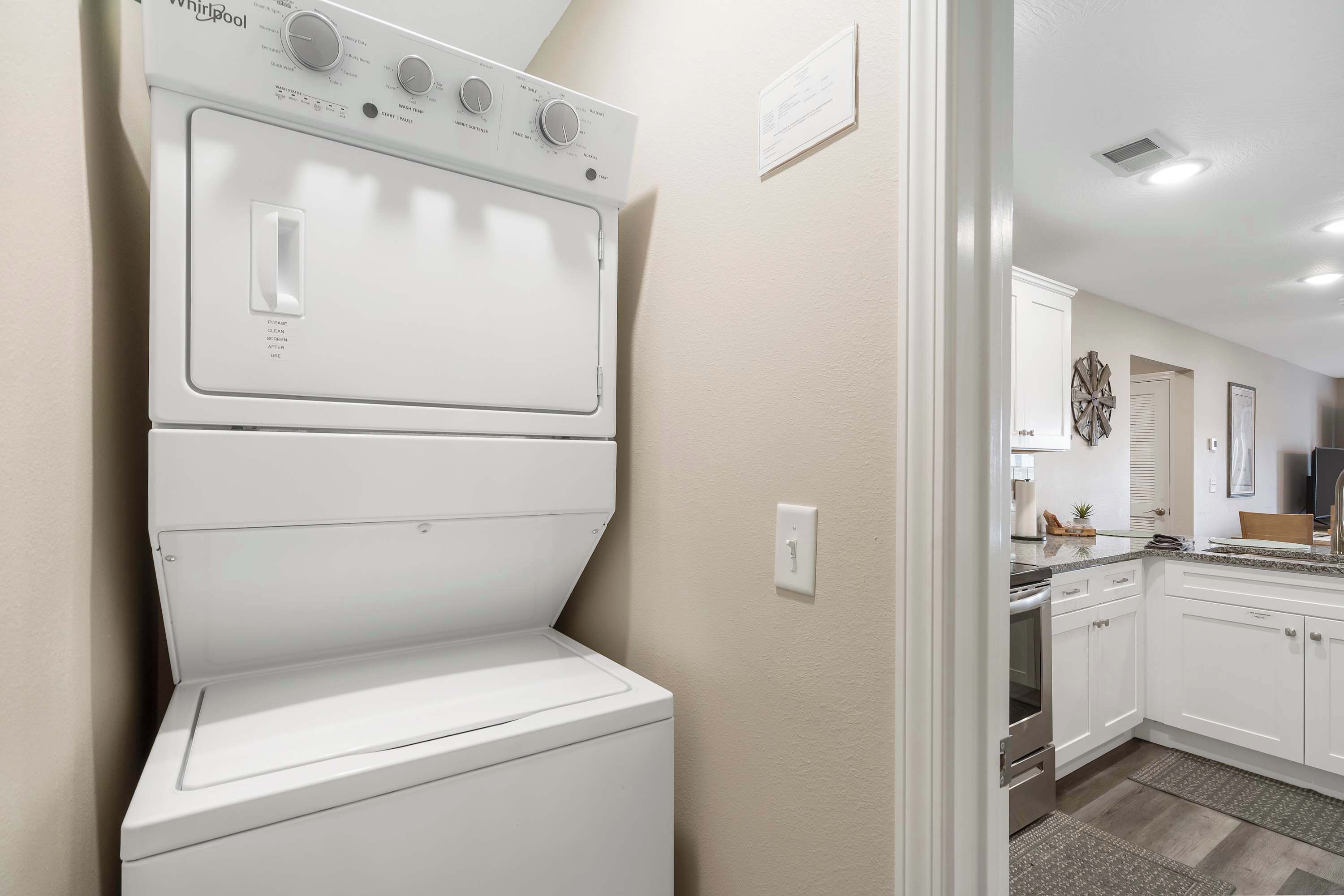 A laundry area with a stacked washer and dryer, a kitchen with white cabinets, and a countertop with a sink and stove.