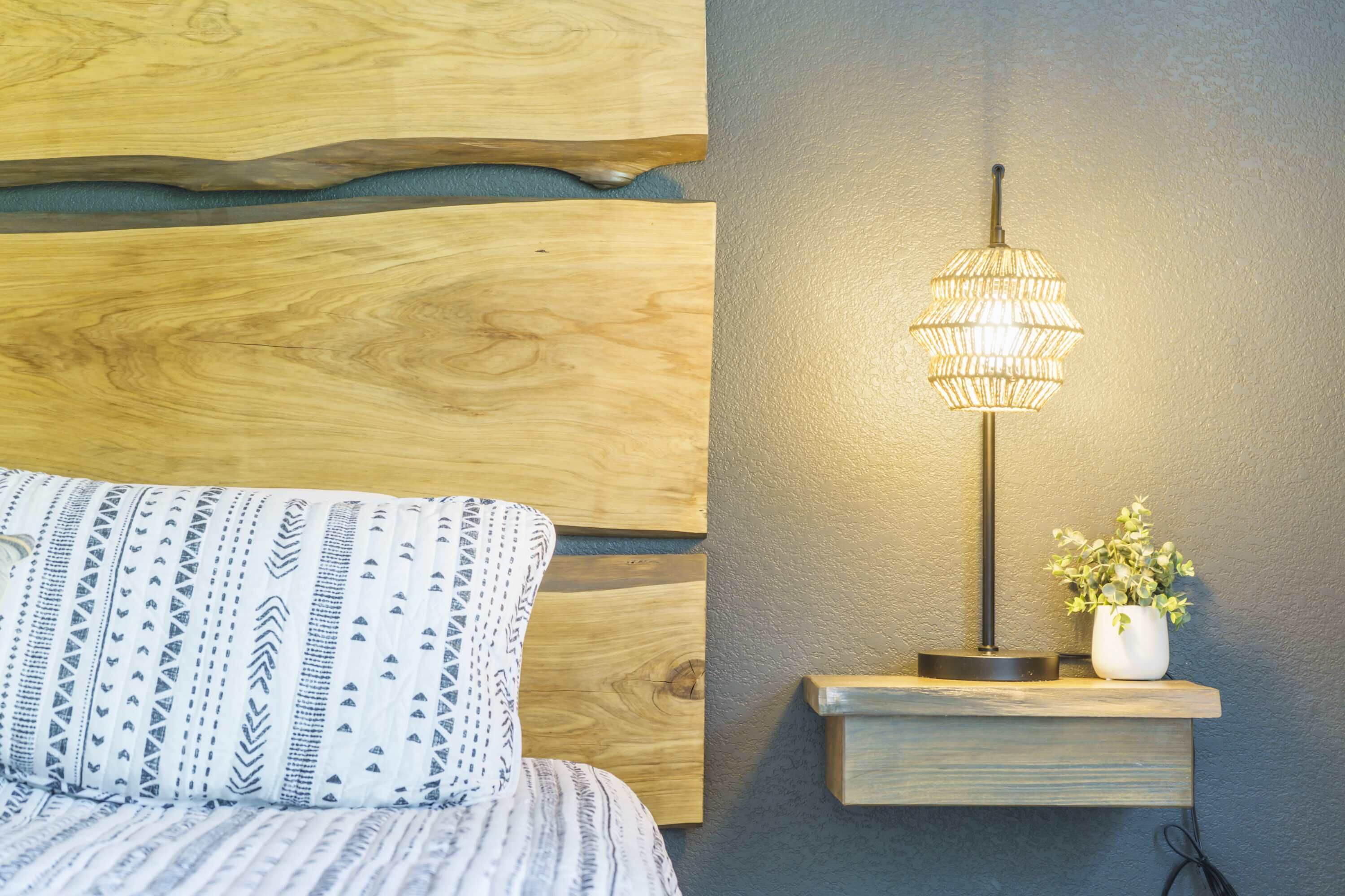 Un letto con lenzuola fantasia, una lampada a parete e una piccola pianta su uno scaffale.