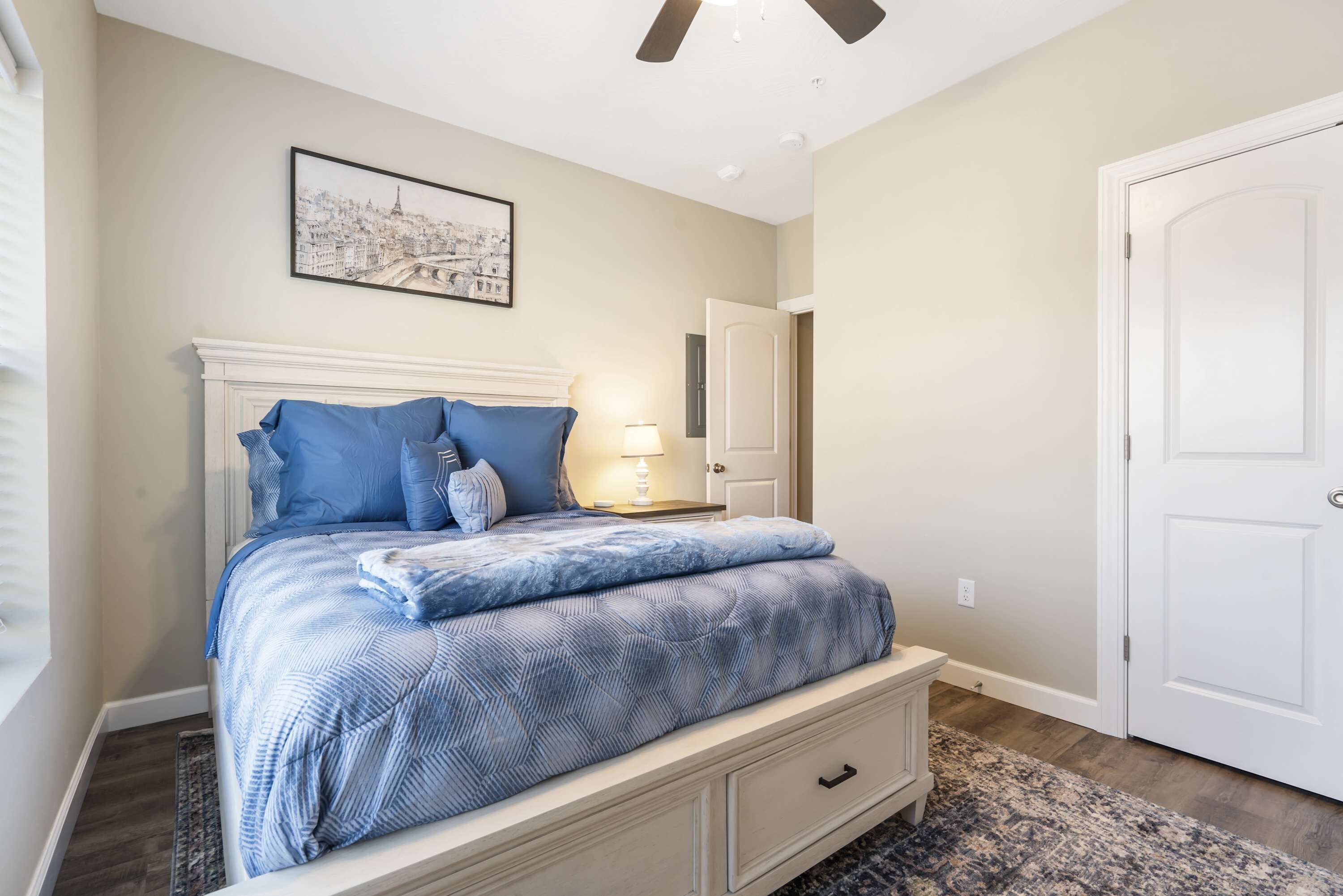 A bedroom with a bed, a nightstand, a lamp, a door, and a ceiling fan.