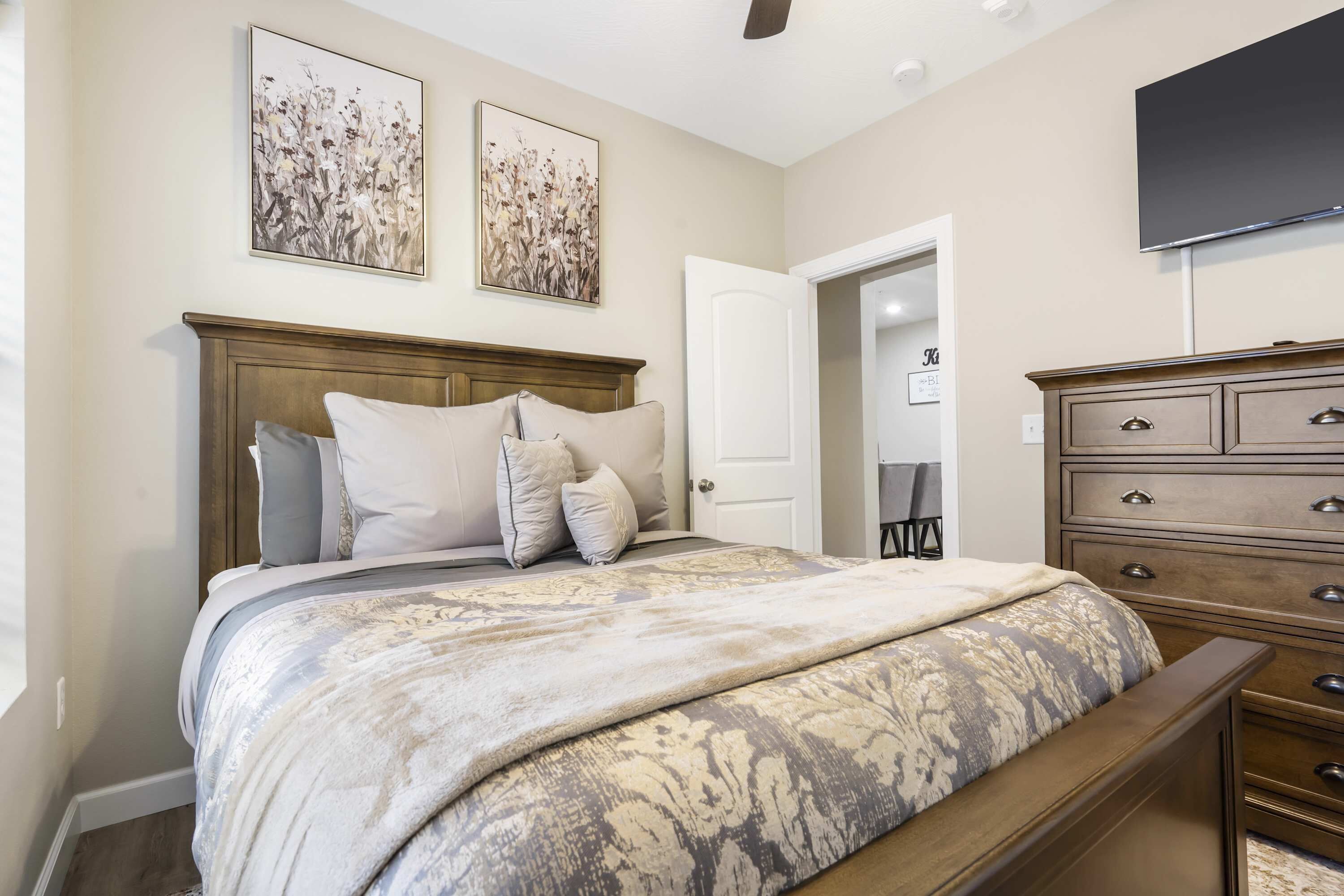 A bedroom with a large bed, a wooden dresser, and two wall-mounted paintings.