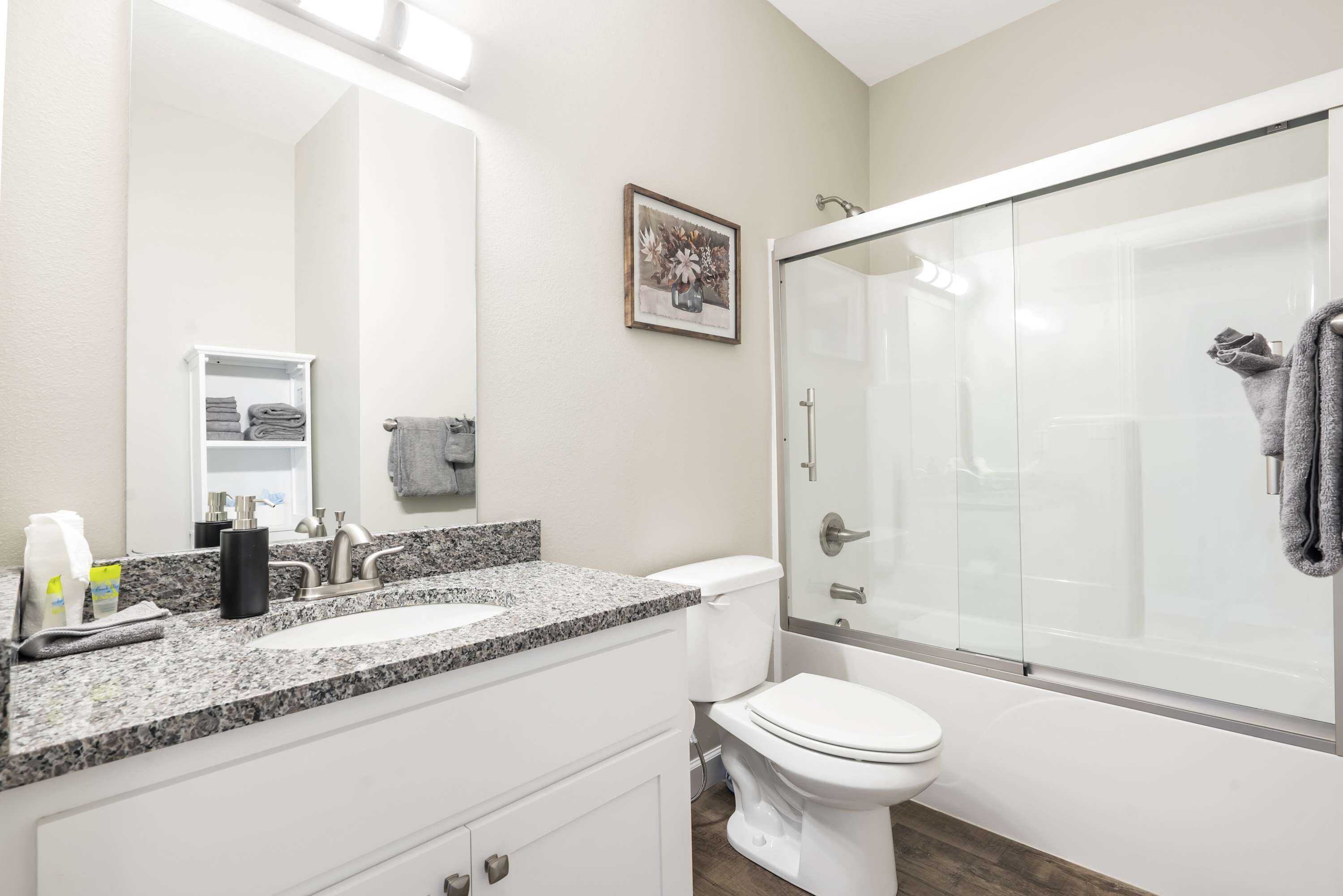 Une salle de bain moderne avec un comptoir en granit, un lavabo blanc et une douche à l’italienne.