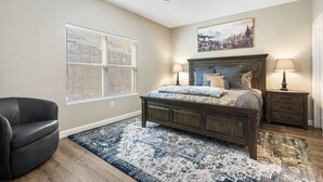 Ein Schlafzimmer mit Bett, Sessel, Nachttisch, Deckenventilator und Fenster mit Jalousien.