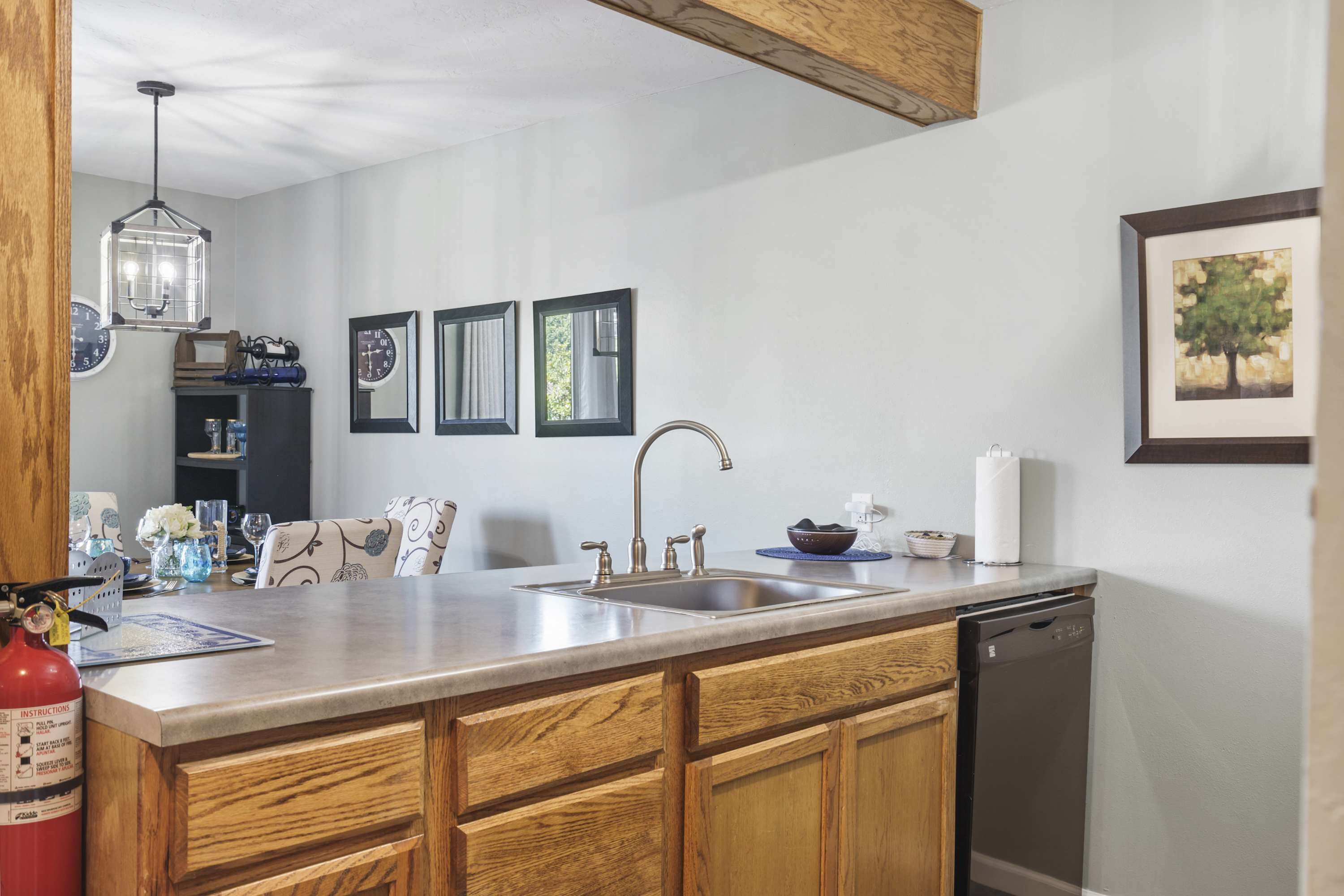 A kitchen with wooden cabinets, a stainless steel sink, a dishwasher, and a pendant light.