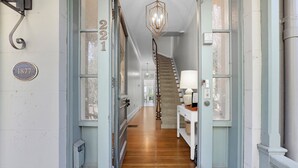 A hallway with a wooden floor, a staircase, and a chandelier.