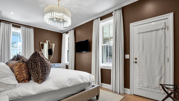 Ein Schlafzimmer mit einem großen Bett, einer Kristallleuchtre, einem Flachbildfernseher und einer Tür, an der ein Handtuch hängt.