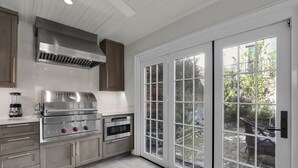 Eine moderne Küche mit Edelstahlgeräten, einem eingebauten Backofen und einer großen Schiebetür zu einer Terrasse.